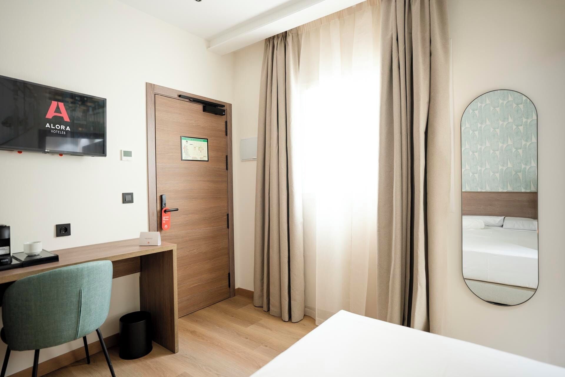 Et hotelværelse med skrivebord, stol, seng og et stort spejl.