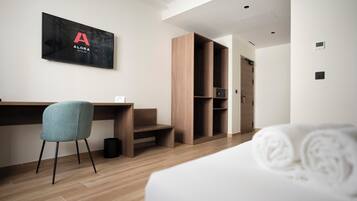 Une chambre d’hôtel équipée d’un lit, d’un bureau, d’une chaise, d’une armoire et d’un téléviseur fixé au mur, sur lequel est affiché le nom de l’hôtel.