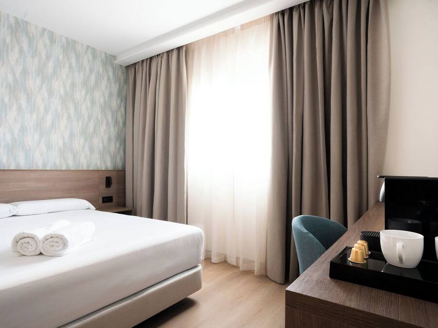 A hotel room with a bed, a desk with a coffee maker, cups, and a TV.