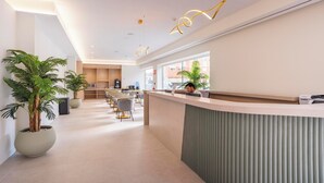 A modern hotel reception area with a long counter, seating, and large windows. - Alora Hotel Mérida  (Mérida)