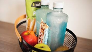 Una cesta con una manzana roja, una manzana verde, un kiwi, un paquete de Snat y dos botellas de líquido azul.