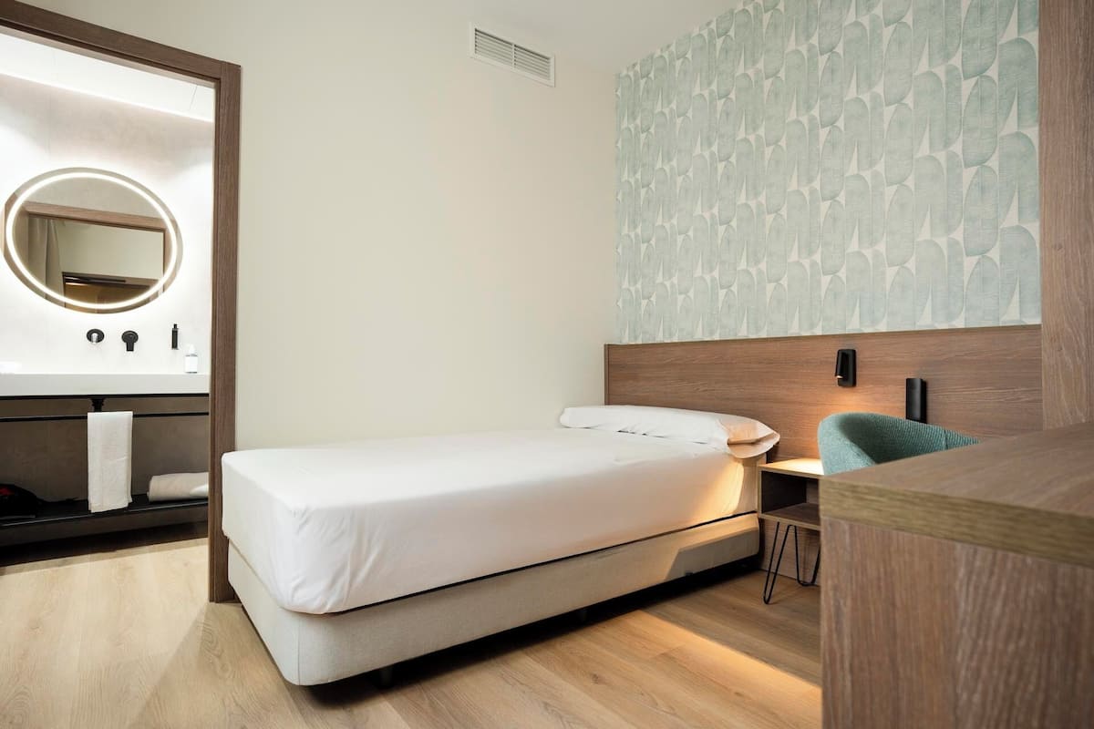 A modern bedroom with a bed, a bedside table, a mirror, and a wall with a leaf pattern.
