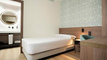 A modern bedroom with a bed, a bedside table, a mirror, and a wall with a leaf pattern.