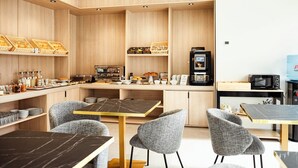 A modern kitchen with wooden cabinets, a coffee machine, and a microwave. There are two tables with chairs, and a water dispenser is visible. - Alora Hotel Mérida  (Mérida)