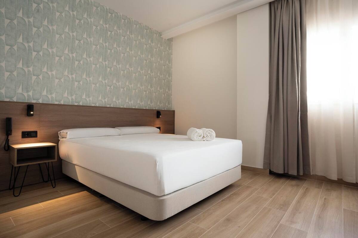 A modern hotel room with a large bed, a bedside table, a wall-mounted phone, and a curtain on the window.