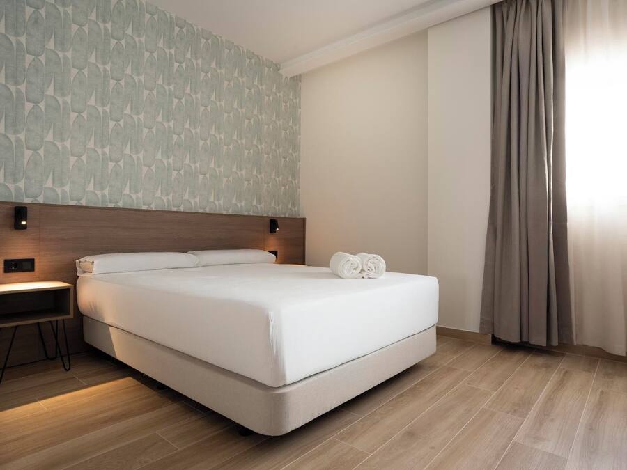 Una habitación de hotel moderna con una cama grande, una mesita de noche, un teléfono en la pared y una cortina en la ventana.