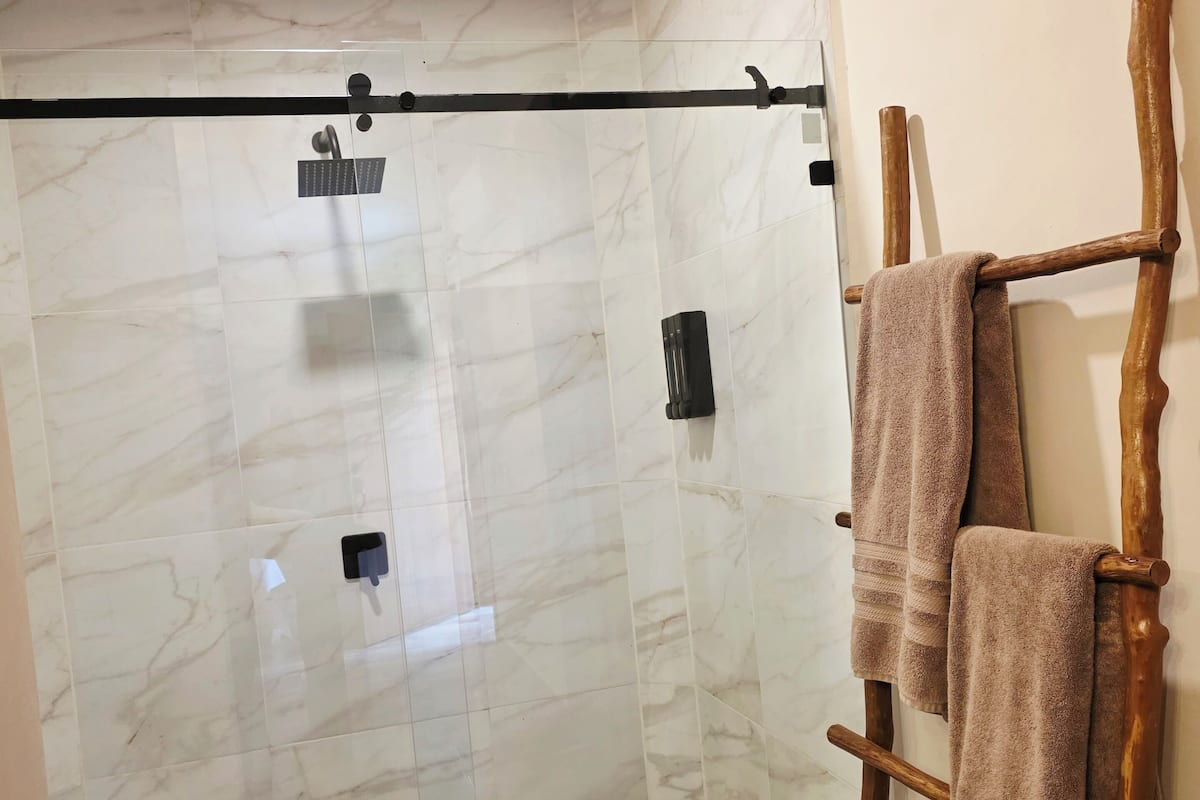 A shower with a glass door, a wooden towel rack, and a marble-tiled wall.