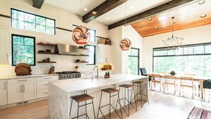 A modern kitchen with a large island, bar stools, and a dining area with wooden chairs. - This idyllic Suncadia home features a speakeasy, cowboy cold dip, outdoor shower, private library, chef's kitchen, golf course views, and MORE (Cle Elum)