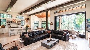 A spacious living room with a black leather sofa, a coffee table, and a large window offering a view of the outdoors. - This idyllic Suncadia home features a speakeasy, cowboy cold dip, outdoor shower, private library, chef's kitchen, golf course views, and MORE (Cle Elum)