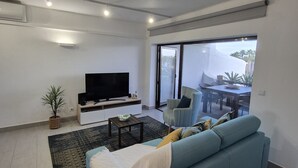 Un saló modern amb un sofà, televisió i una zona de menjador visible a través d'una porta de vidre.