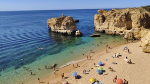 A beach with clear water, rocky formations, and people sunbathing.