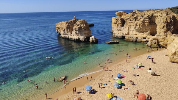 A beach with clear water, rocky formations, and people sunbathing.