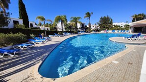 Una piscina amb gandules blaves, palmeres i edificis blancs al fons.