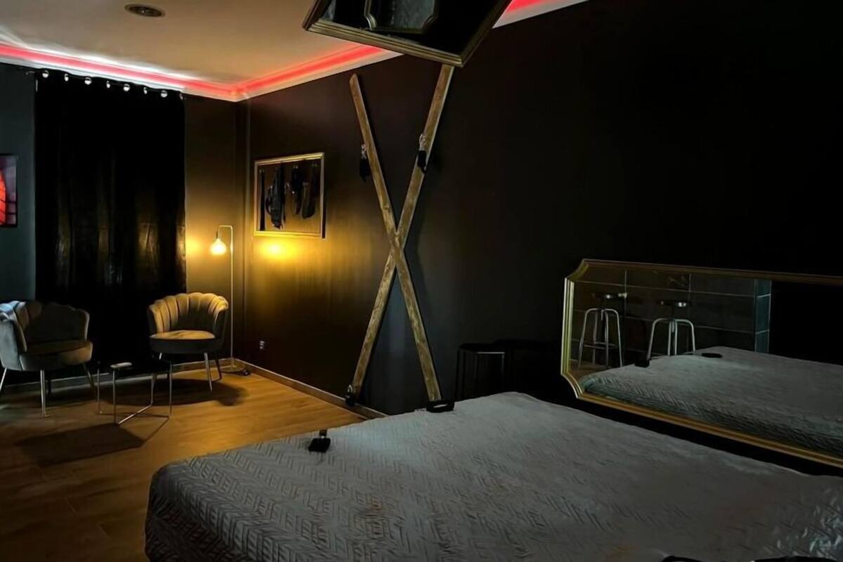 A hotel room with a bed, two chairs, a standing lamp, and a mirror on the wall.