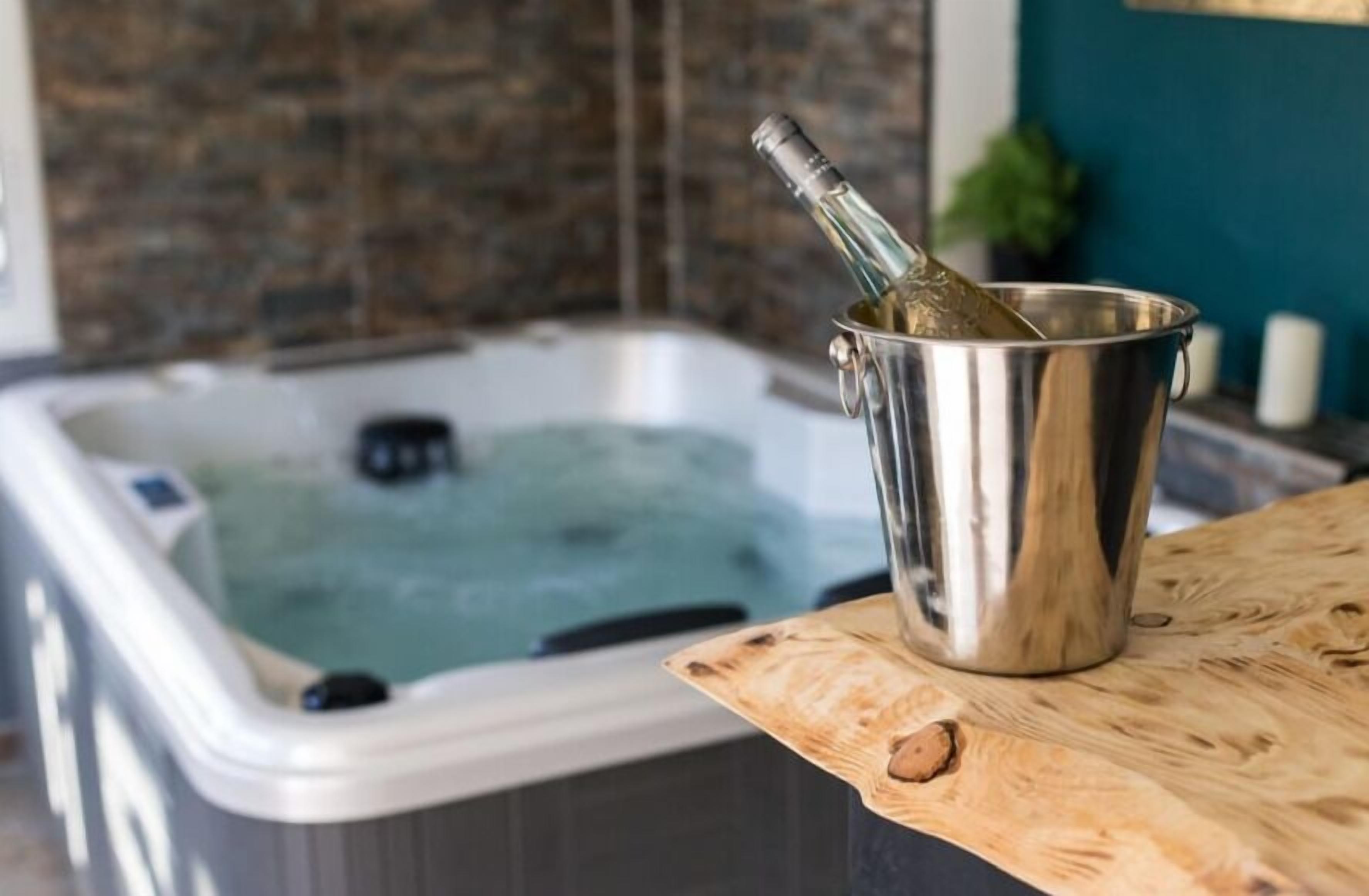 A hot tub with a bottle of champagne in a metal bucket on a wooden table.