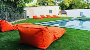 Una piscina con cojines naranja y una pared blanca al fondo.