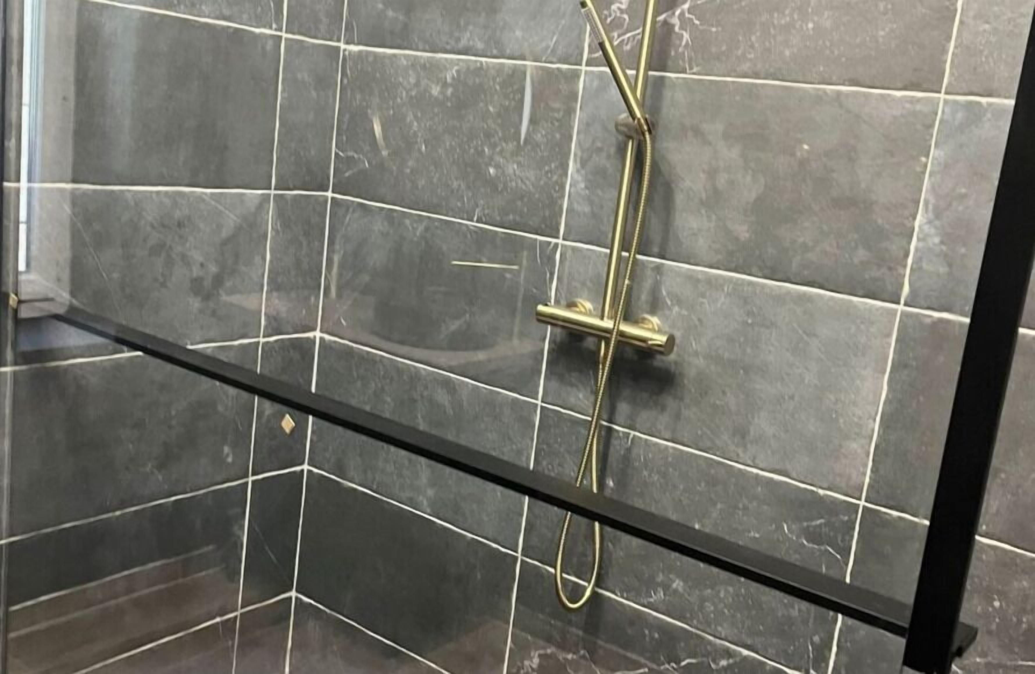 Cabina doccia con pareti piastrellate scure e un divisorio in vetro.