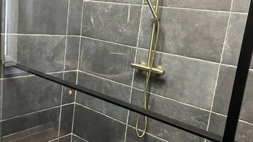Cabina doccia con pareti piastrellate scure e un divisorio in vetro.