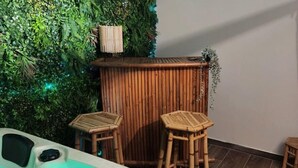 Zona de spa con un jacuzzi, dos taburetes de madera y una pared de bambú con vegetación.