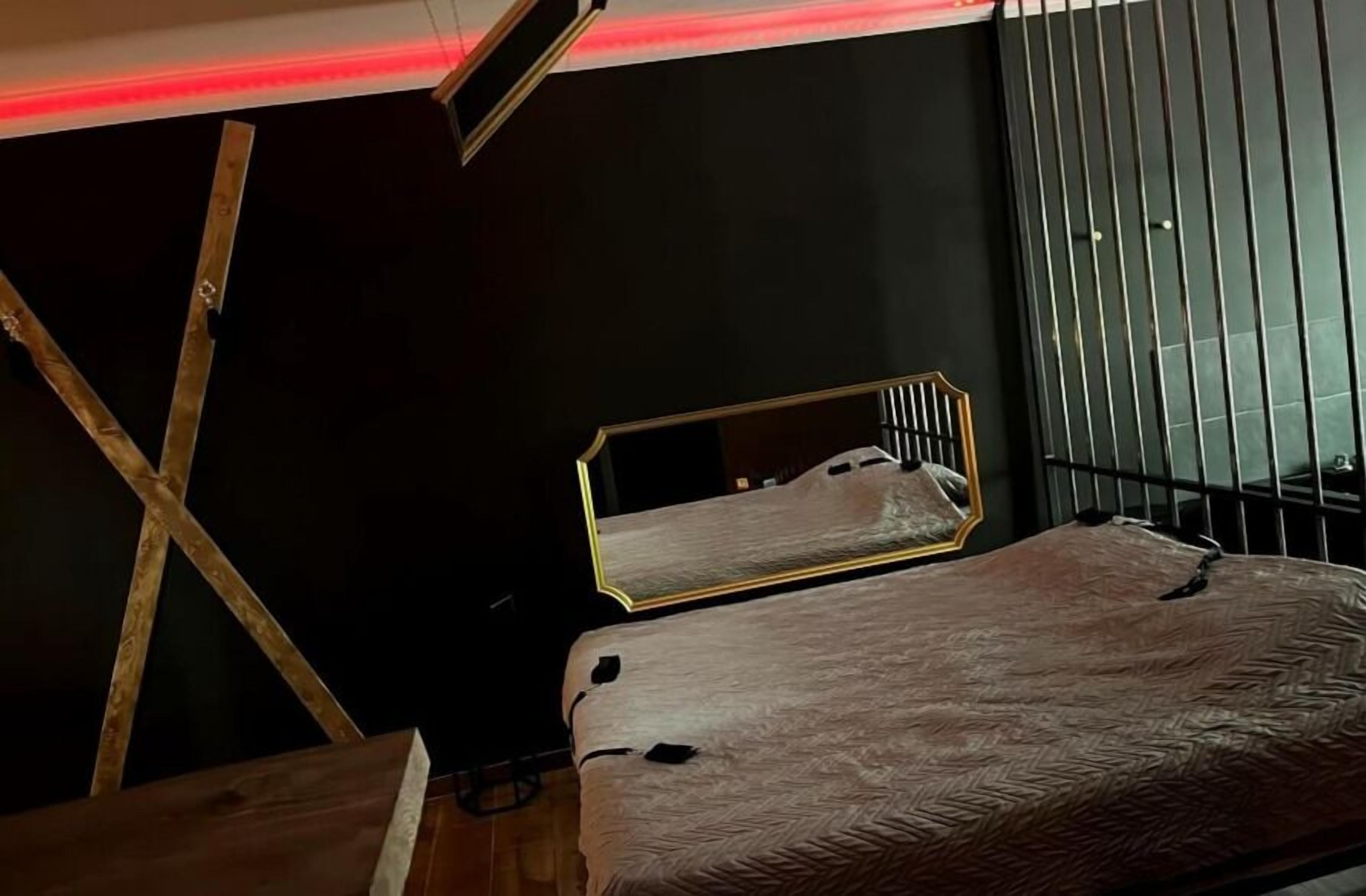 A bedroom with a bed, a mirror, and a window with vertical blinds.