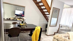 A dining area with a TV, a clock, and a staircase. - Duke Mews Loft: Cozy 1-Bedroom Apartment in Sandton: 15 Mins to Sandton City. (Sandton)