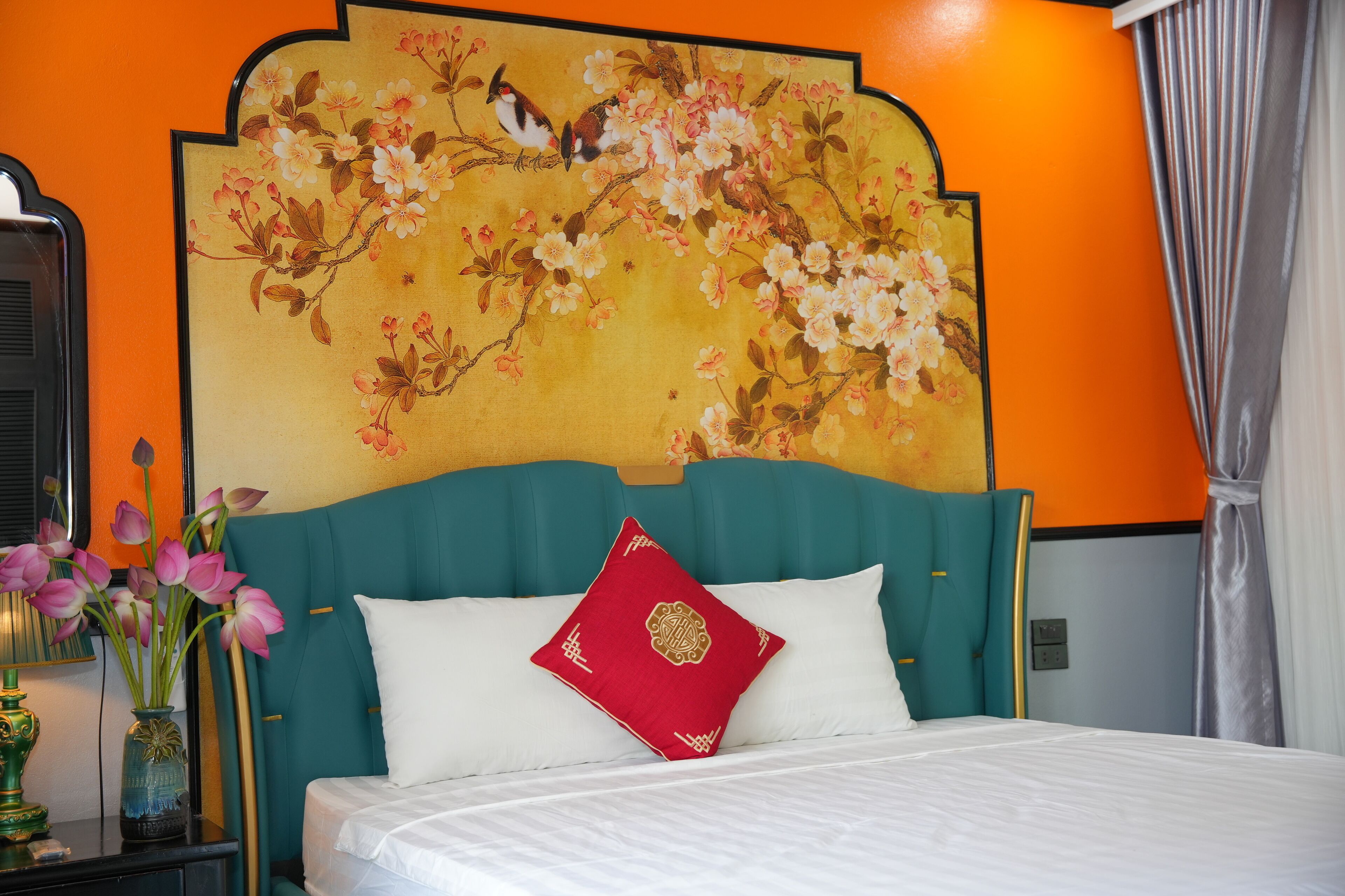 Een hotelkamer met een bed, een rood kussen, een vaas met bloemen en een wanddecoratie.