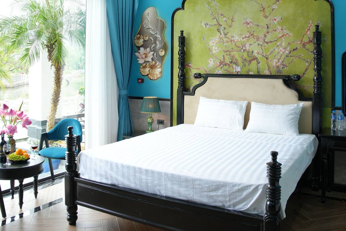 Un dormitorio con una cama, ventilador de techo, ventana con cortinas, una palmera y un adorno en la pared.
