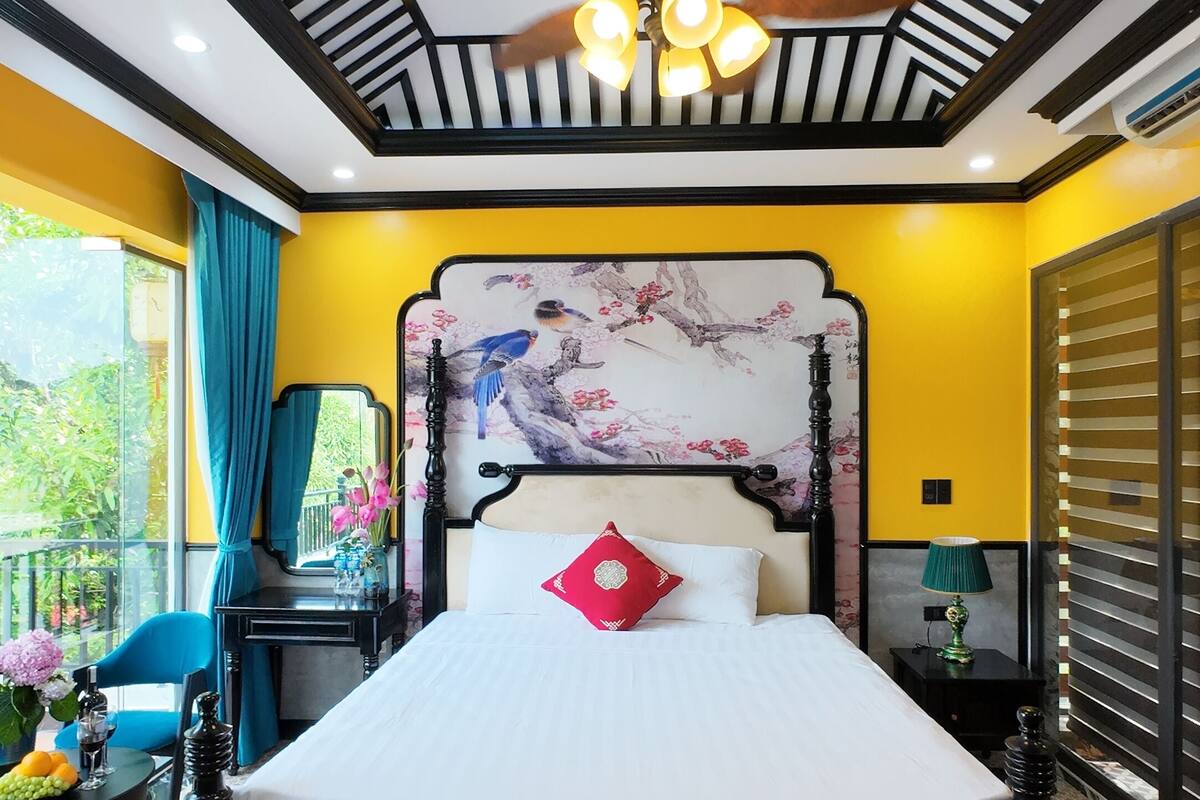 Un dormitorio con una cama, ventilador de techo, mesita de noche, espejo y ventana con cortinas.