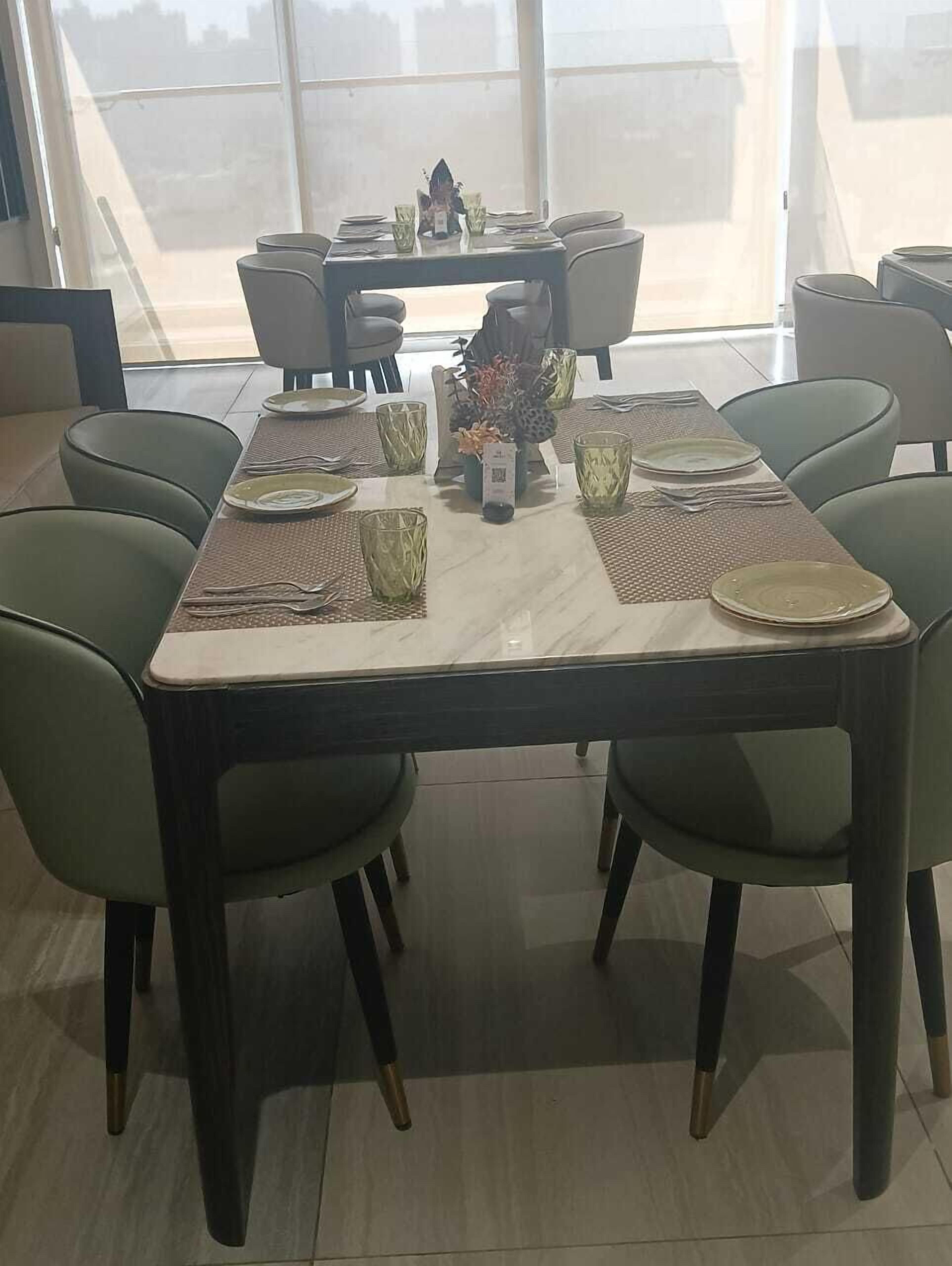 A dining area with a large table set for four, surrounded by green chairs.