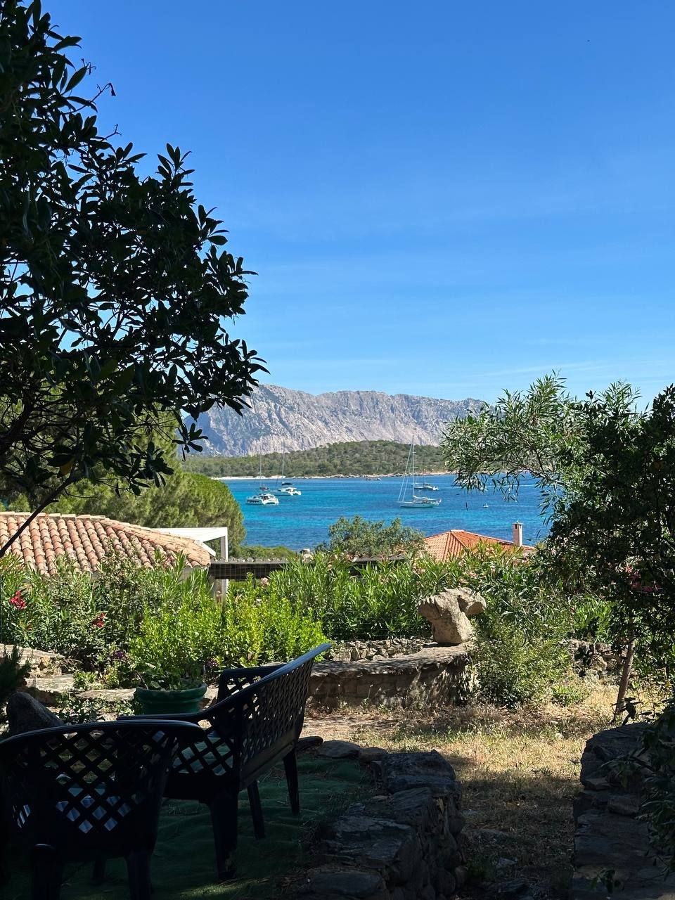 Een terras met tuinmeubilair met uitzicht op de kust, met boten en bergen.