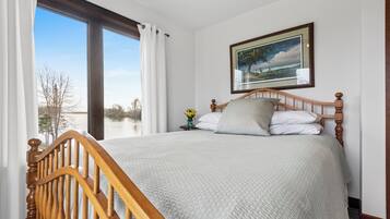 Une chambre avec une grande fenêtre, un lit doté d’une tête de lit en bois et un tableau encadré accroché au mur.