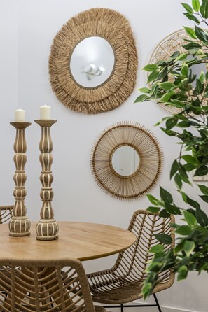 Una mesa de madera redonda con dos velas en soportes, rodeada de sillas de mimbre y un espejo en la pared.