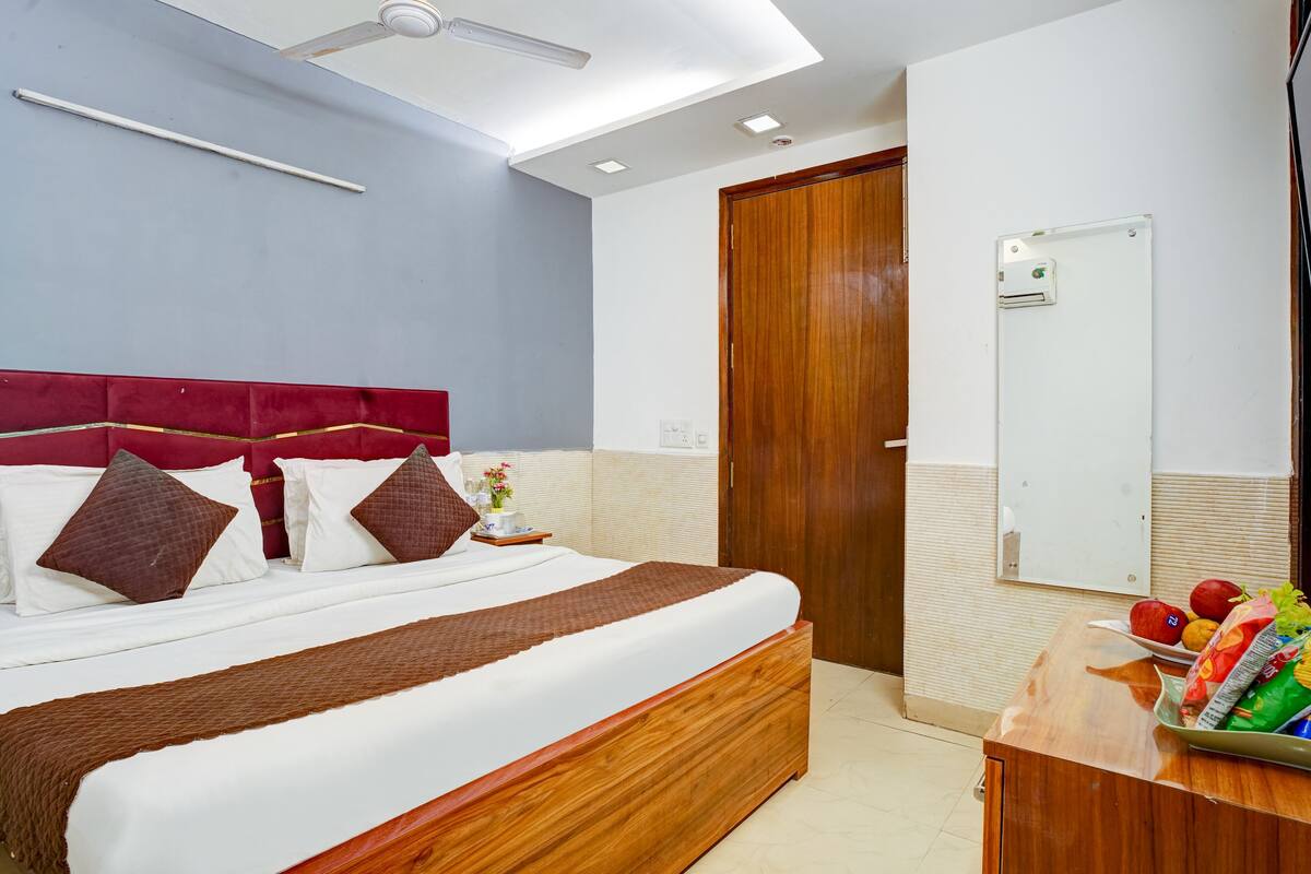 A hotel room with a large bed, a wooden headboard, a ceiling fan, a bedside table with fruit, and a mirror on the wall.