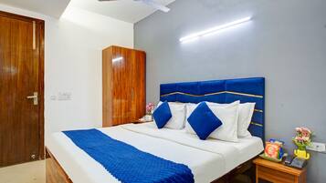 A neatly made bed with a blue blanket, a wooden wardrobe, a bedside table with a vase of flowers, and a ceiling fan.
