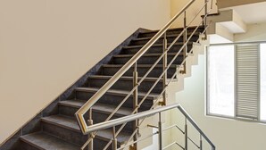 A modern staircase with metal railings and dark steps, leading to a landing area with a window. - Hotel Black Rose (New Delhi)