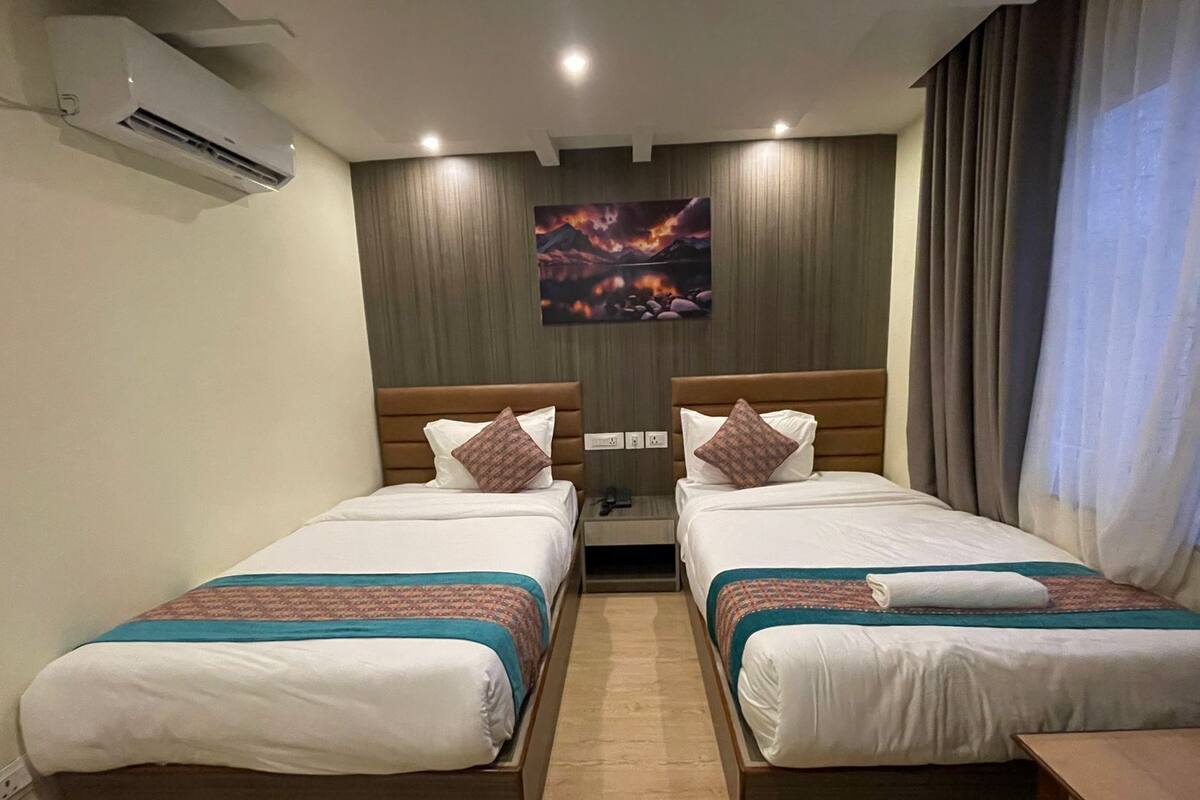 A hotel room with two beds, a painting on the wall, and an air conditioning unit.