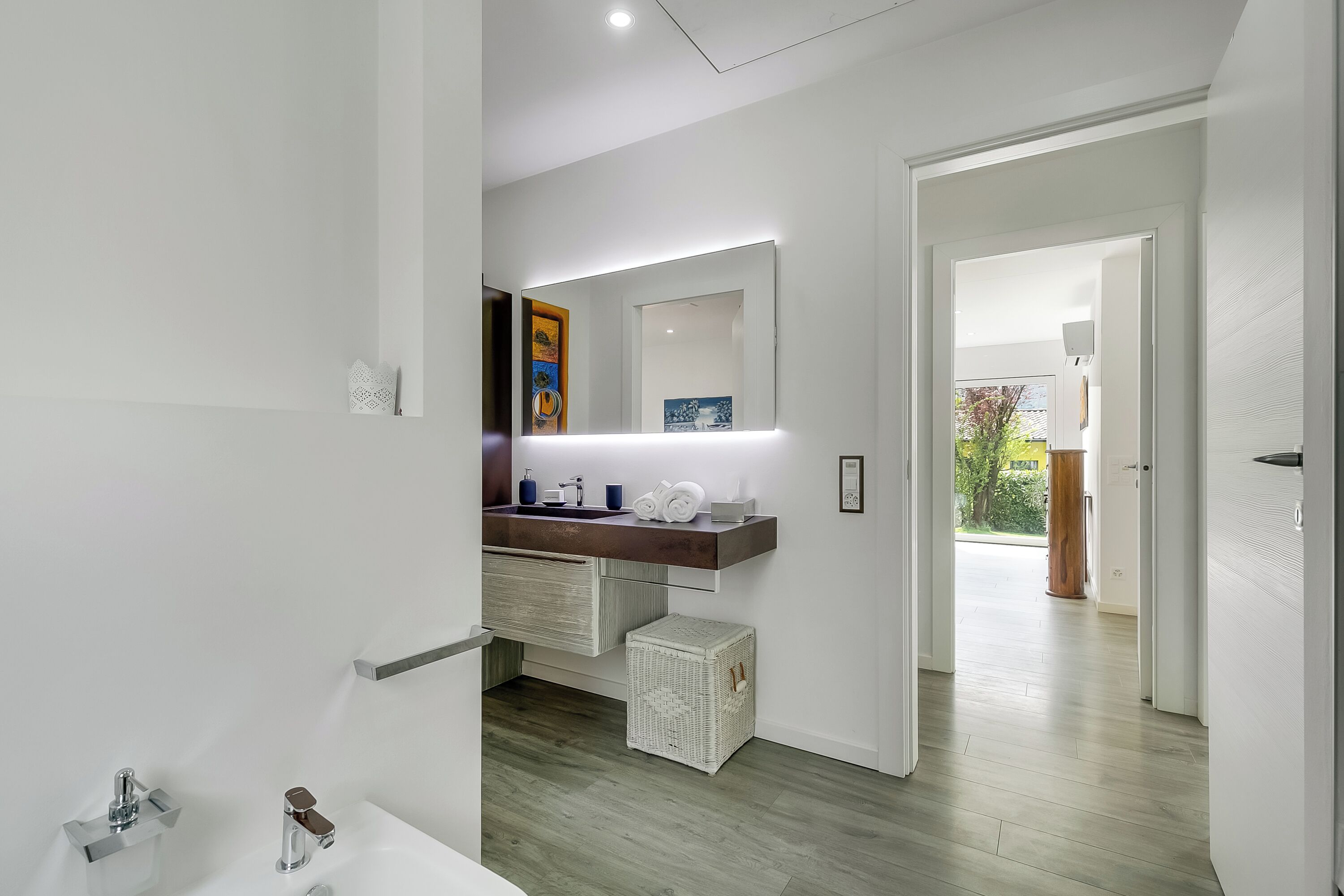 A modern bathroom with a white sink, a mirror, and a wooden vanity.