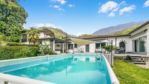A rectangular swimming pool with a white deck, surrounded by lush greenery and a mountain backdrop. - La Rotonda Villa With Pool and Jacuzzi (Maroggia)