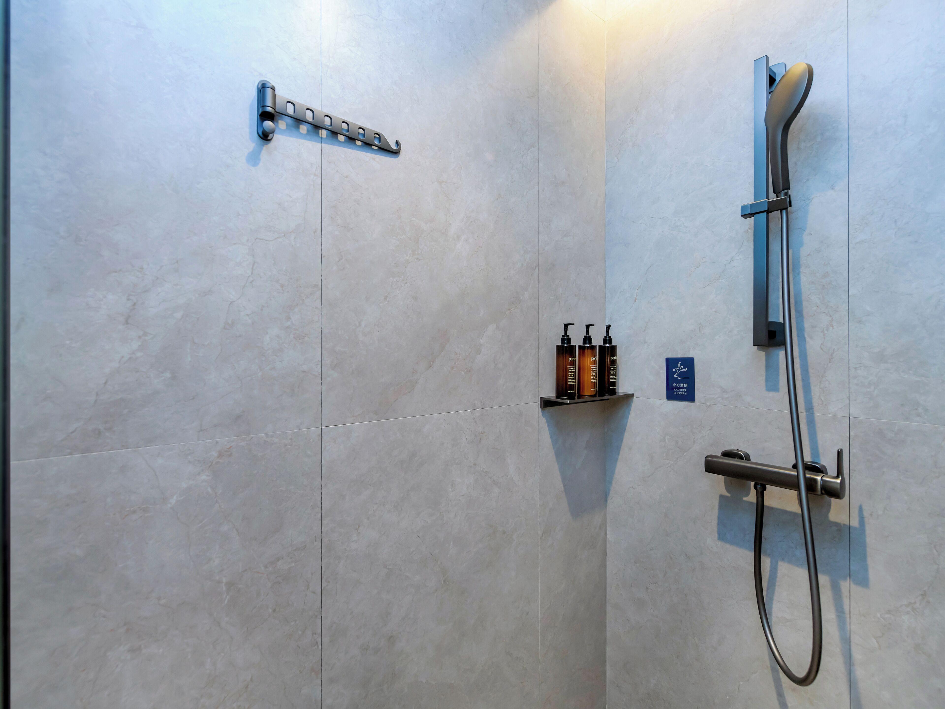 A bathroom with a shower, a towel rack, and a shelf with toiletries.