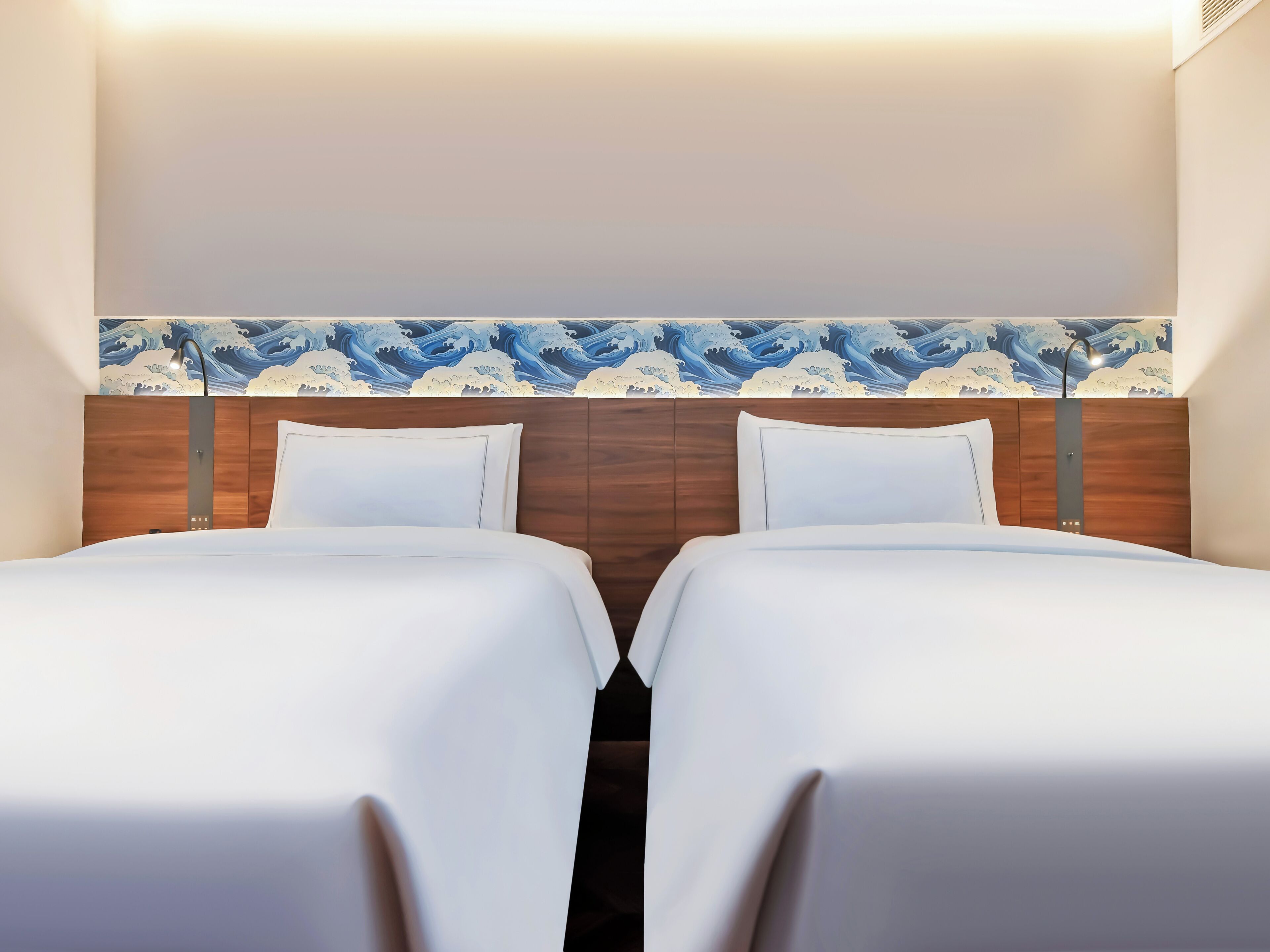 A hotel room with two beds, a wooden headboard, and a wave-patterned wallpaper.