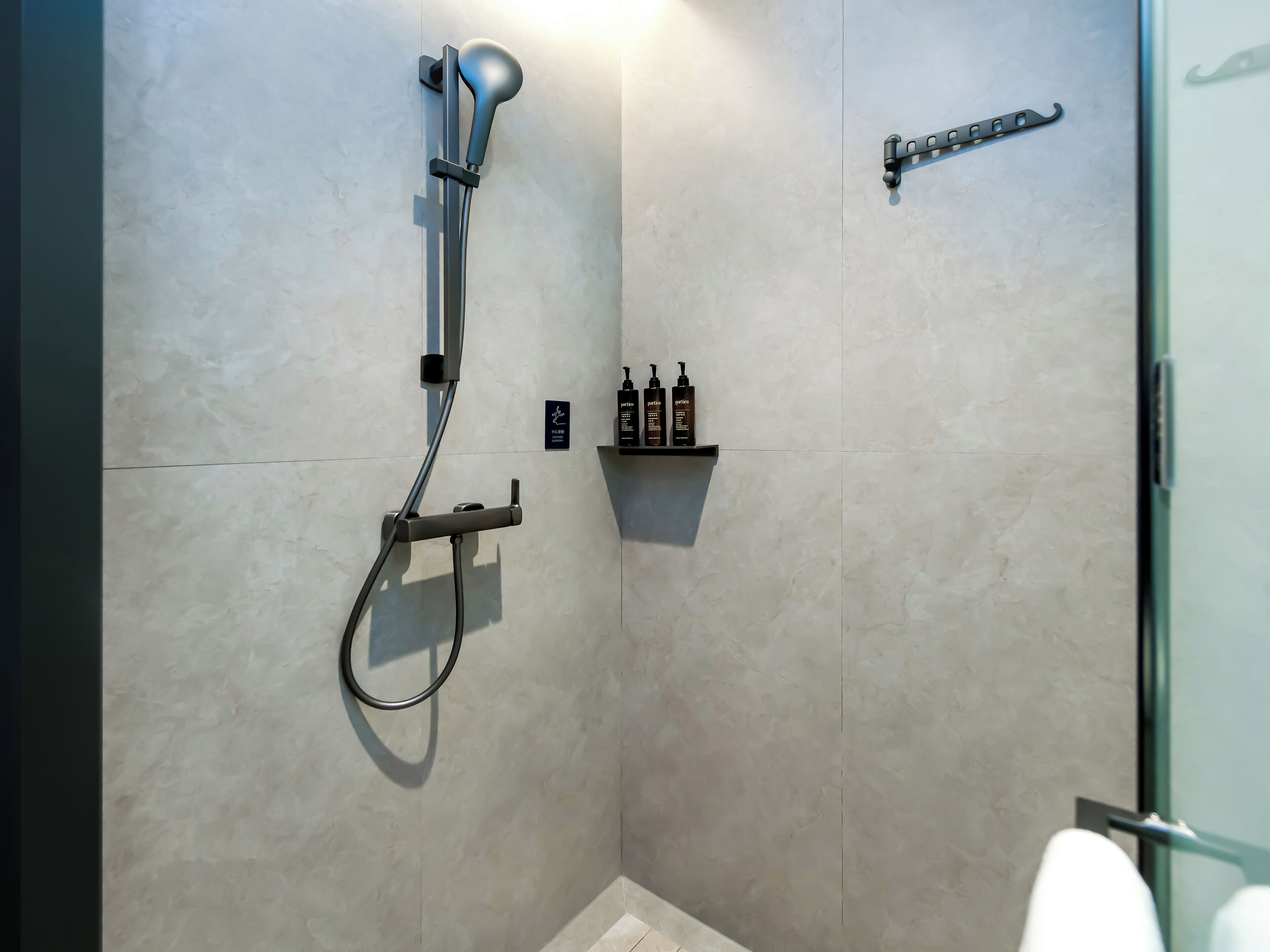A modern shower with a handheld showerhead, a wall-mounted faucet, and a shelf with toiletries.
