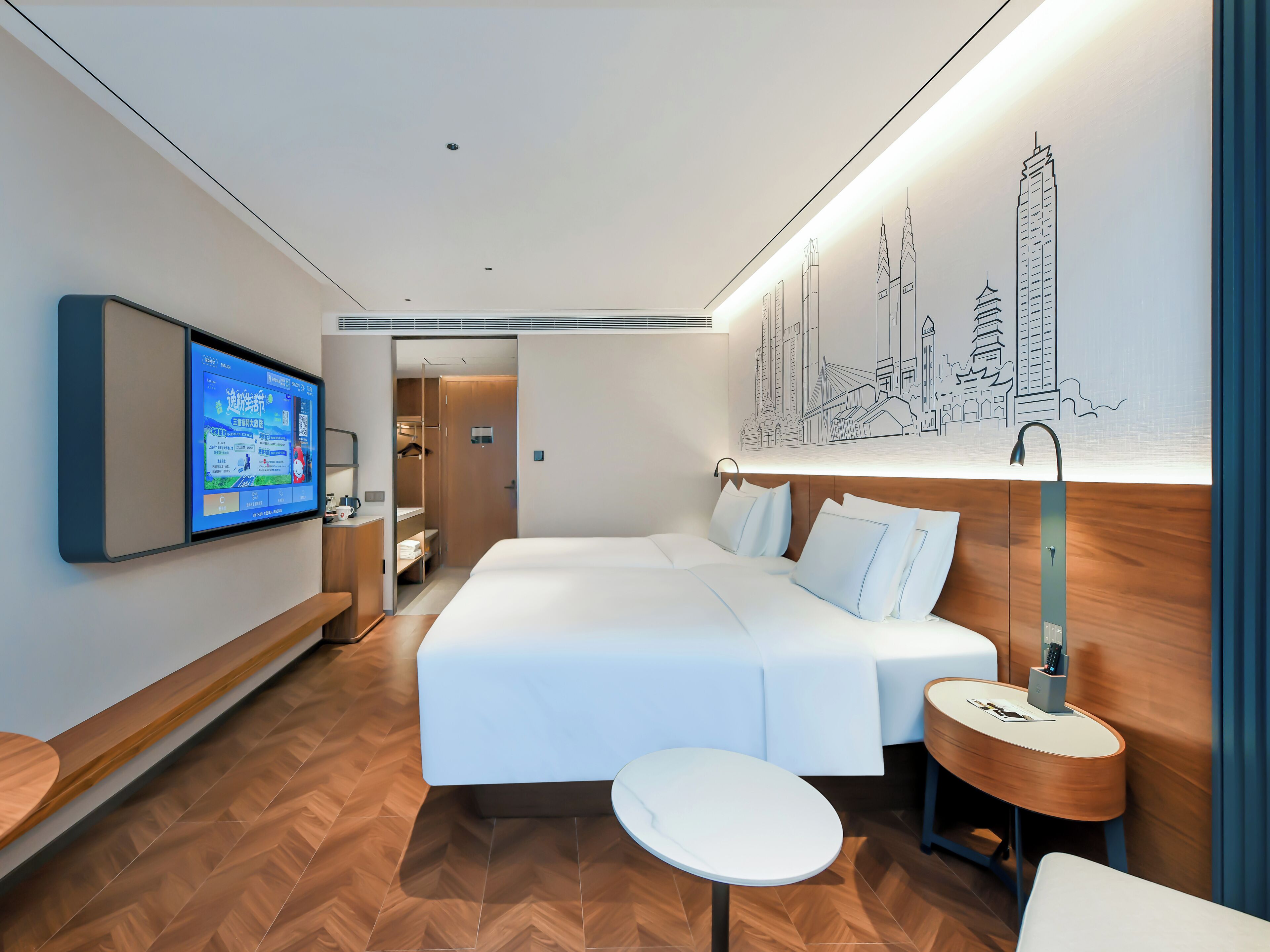 A modern hotel room with a bed, bedside table, lamp, and a wall-mounted TV.
