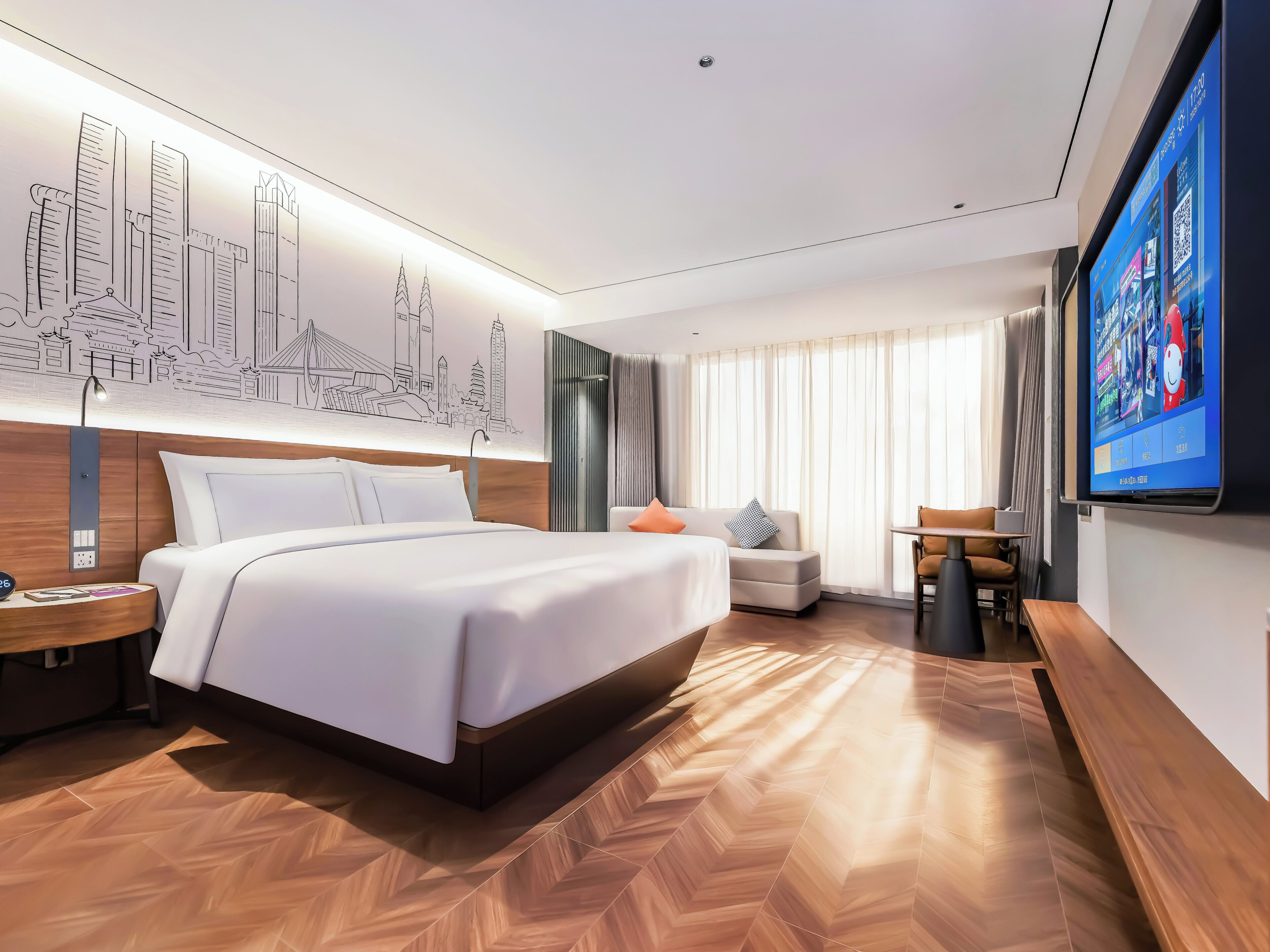 A modern hotel room with a large bed, a desk, a TV, and a cityscape mural on the wall.