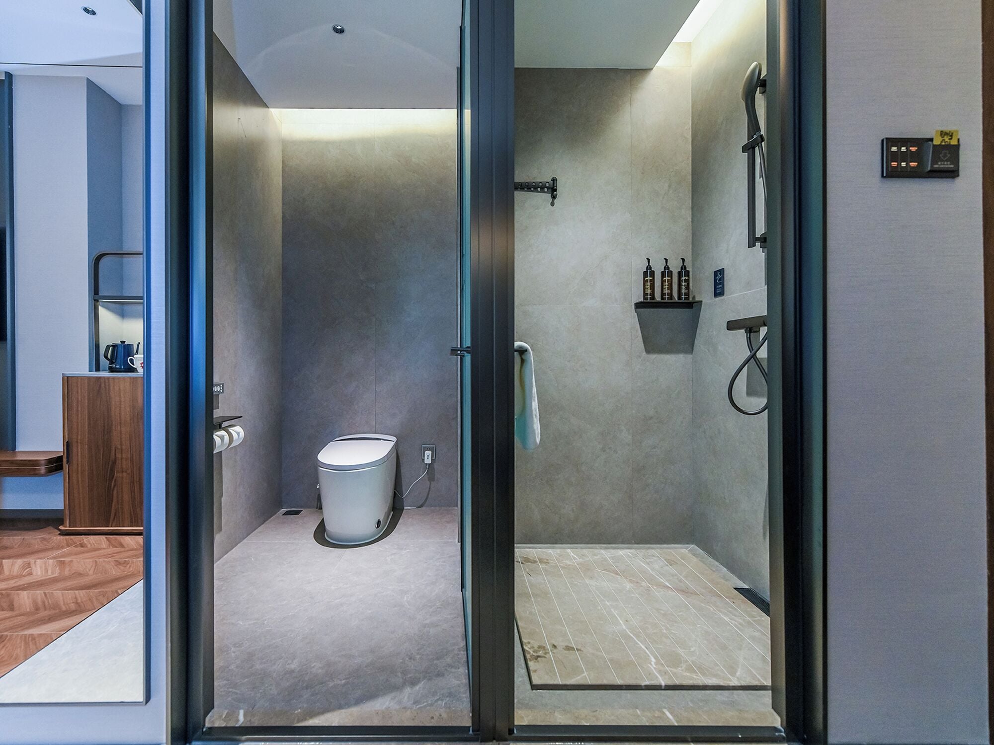 A modern bathroom with a glass shower enclosure, a toilet, and a small shelf with toiletries.