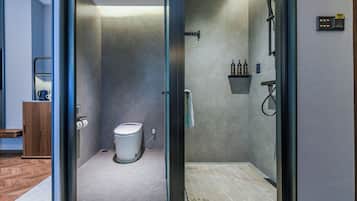 Un baño moderno con cabina de ducha de vidrio, inodoro y estante pequeño con artículos de tocador.