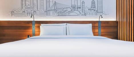 Una cama con ropa de cama blanca, cabecera de madera y un mural en la pared con el horizonte de una ciudad.