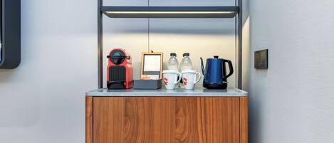 A wooden cabinet with a metal shelf containing a red appliance, a framed document, two water bottles, and a blue kettle.