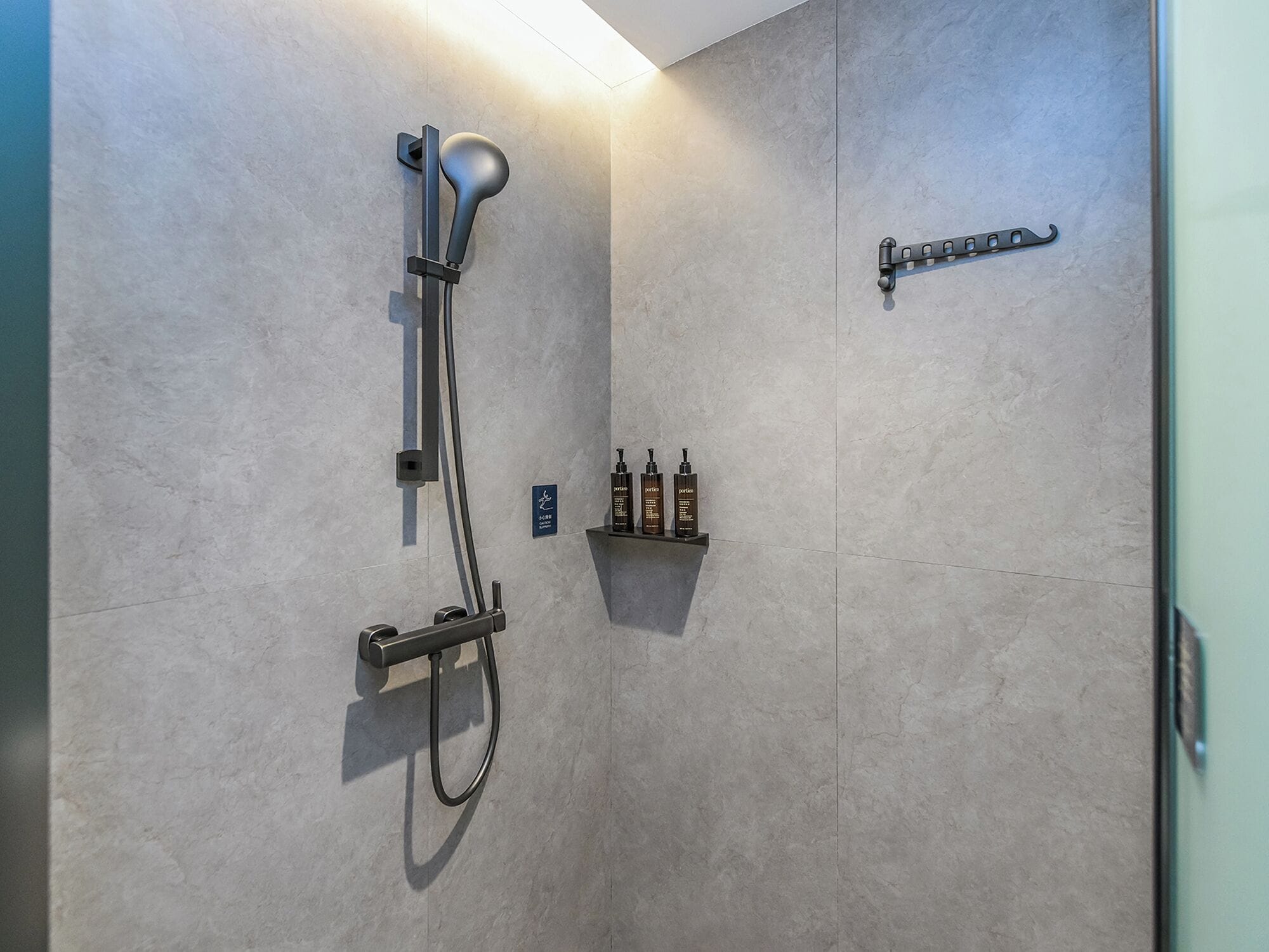 A modern shower with a handheld showerhead, a wall-mounted control panel, and a shelf with toiletries.