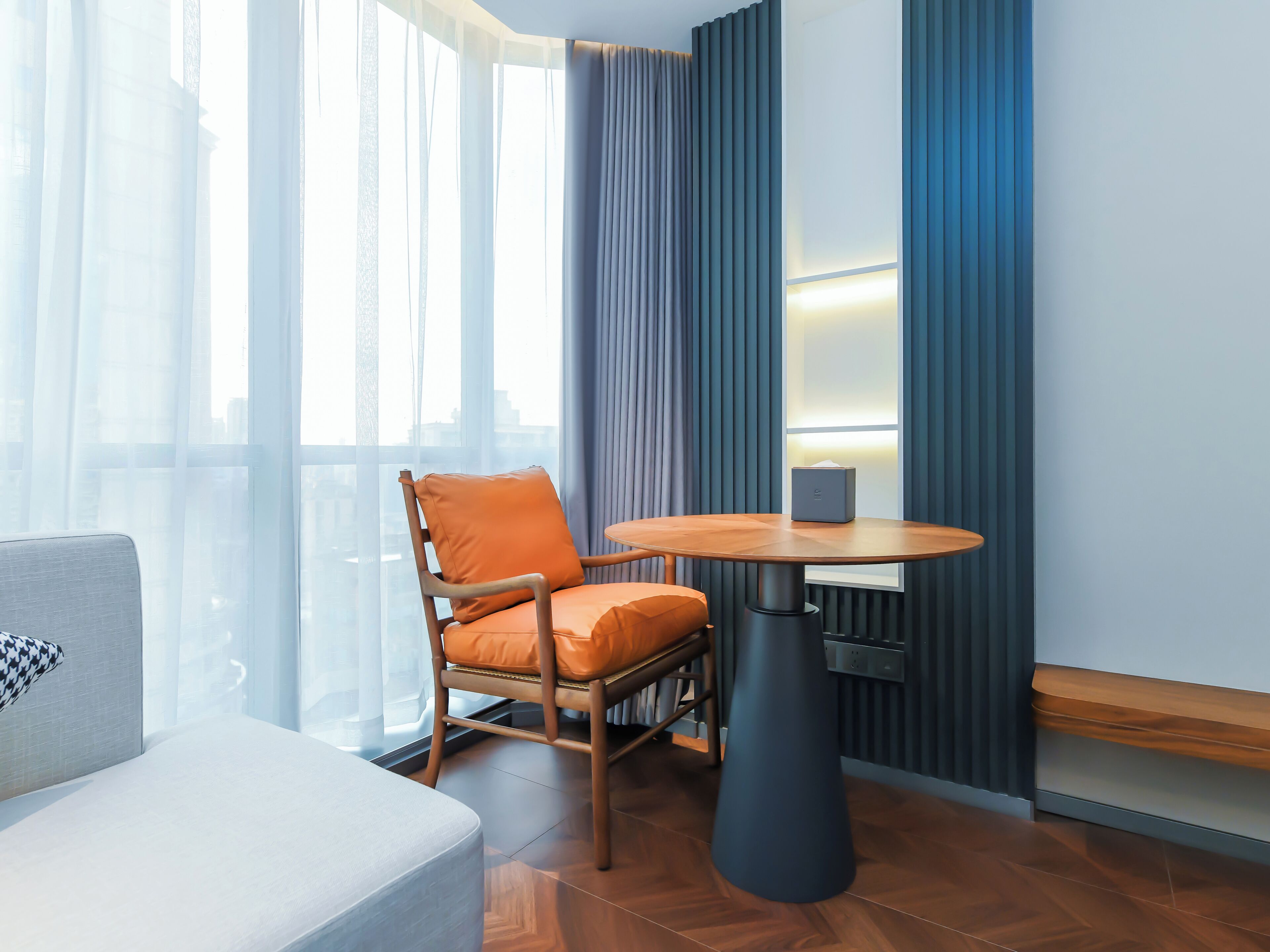 A modern hotel room with a wooden chair, a round table, and a sofa.