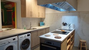 Eine moderne Küche mit Holdekor-Schränken, einer Edelstahl-Dunstabzugshaube, einer integrierten Waschmaschine und einer Arbeitsplatte mit Kaffeemaschine und Geschirr.